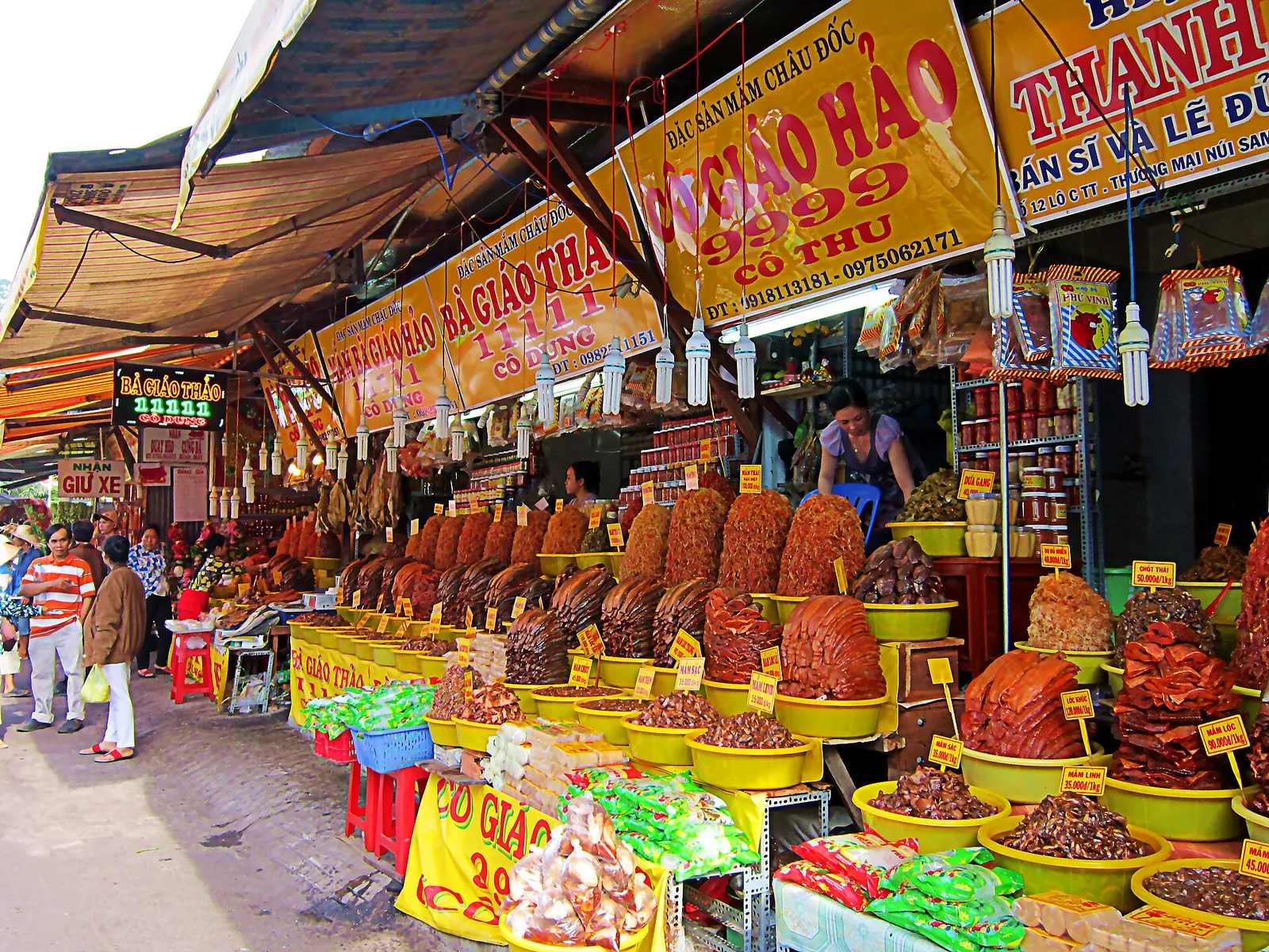 Market stall in Chau Doc piled with trays of red-brown fermented fish (mắm) under shop signs