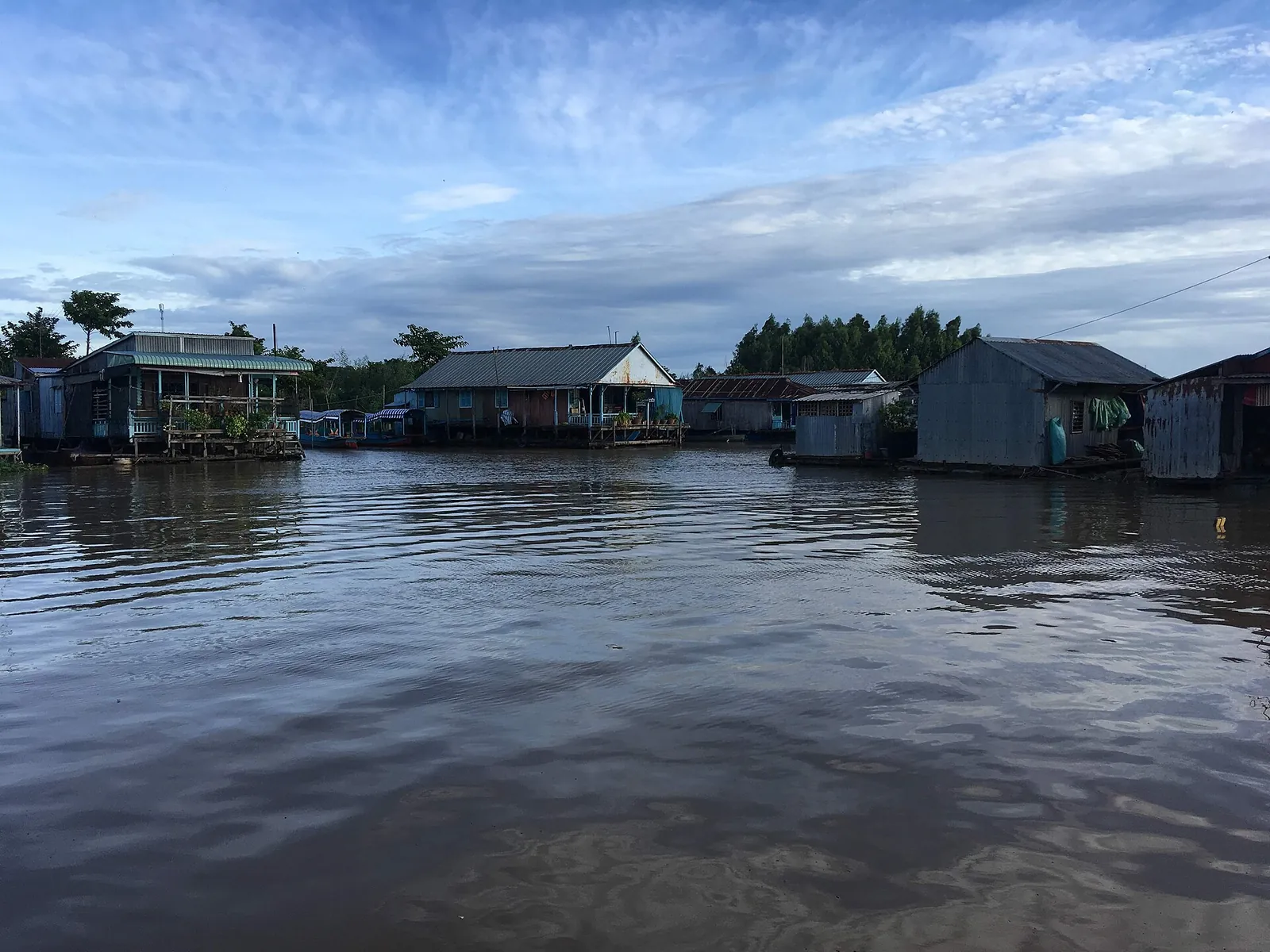 Wooden houses on rafts floating on the wide brown Hau River under a cloudy sky