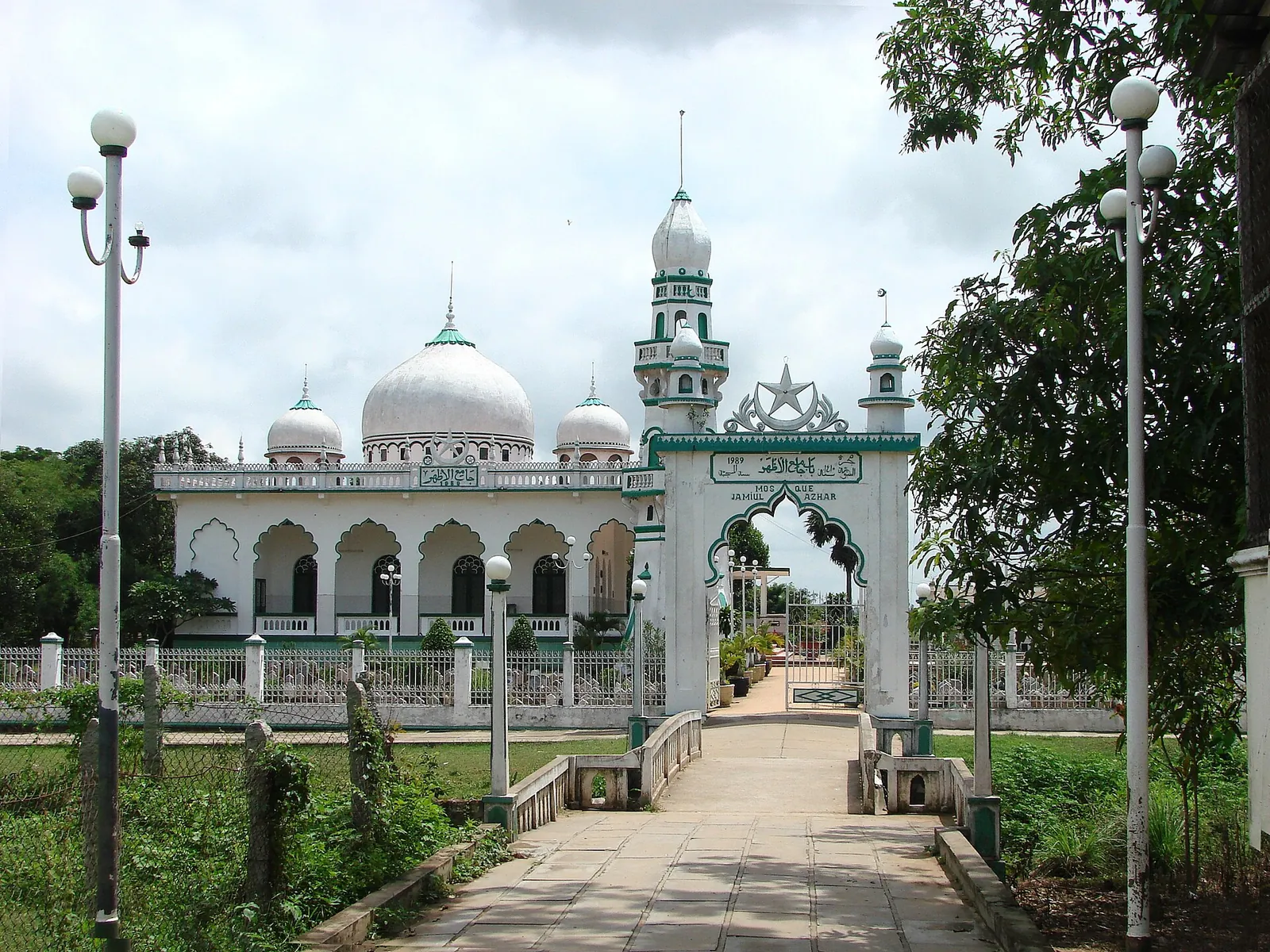 White mosque with domes and a slender minaret behind a garden path