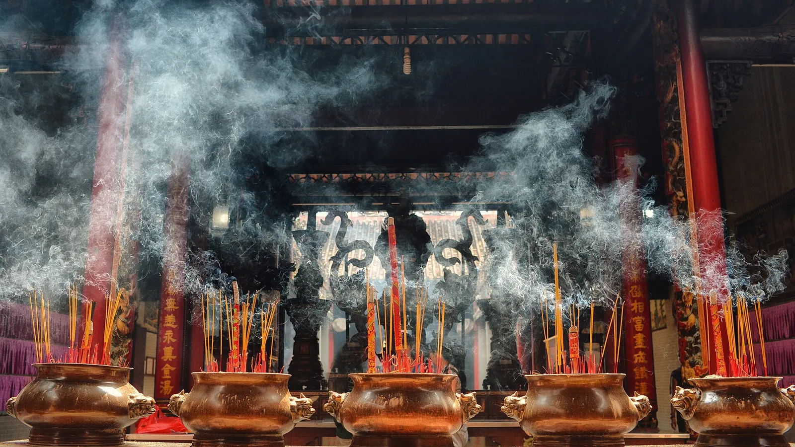 Large bronze incense burners with burning incense sticks and smoke inside Thien Hau Temple