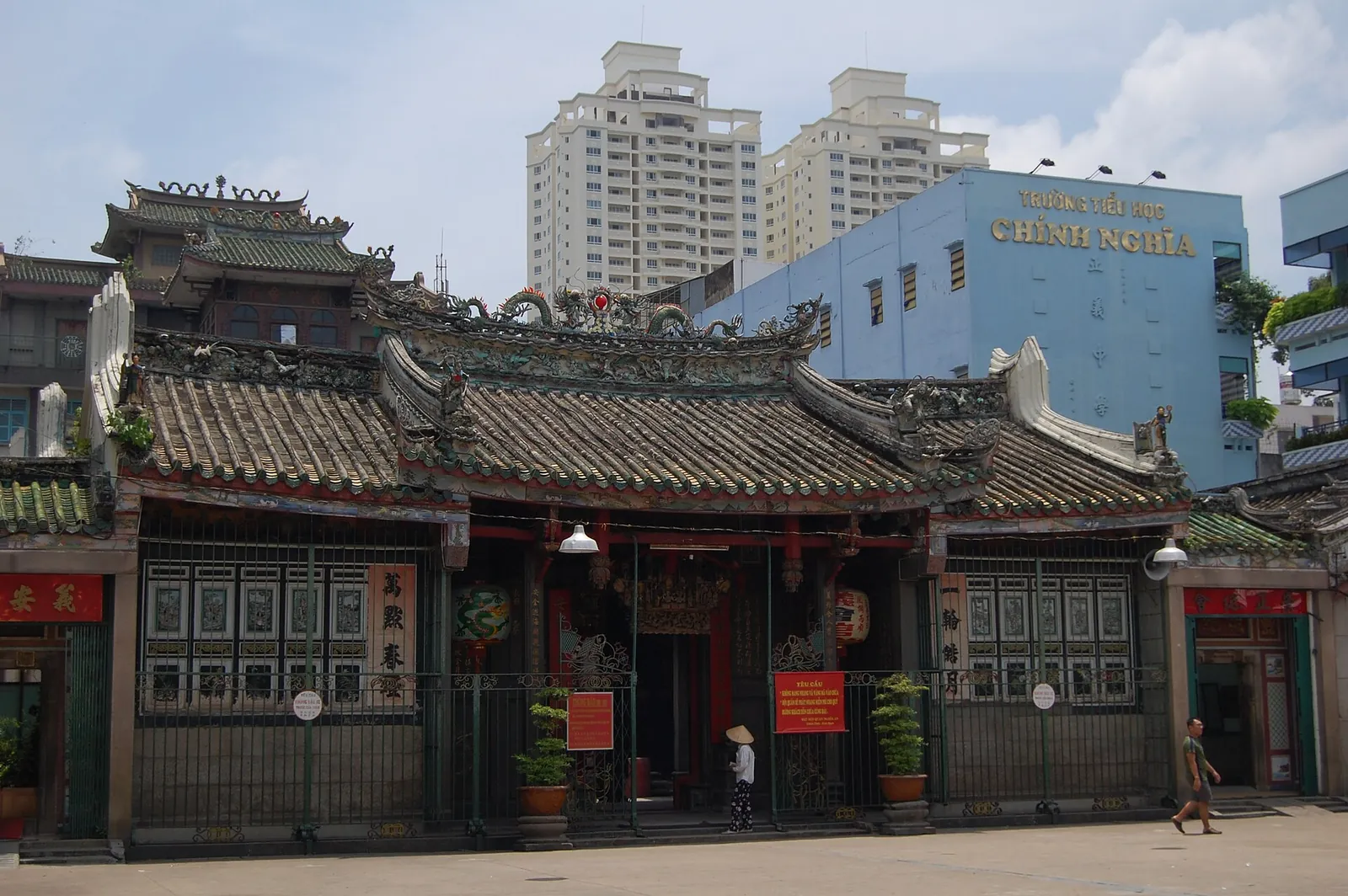 The low tiled roofs and carved facade of Nghia An Assembly Hall with apartment towers behind