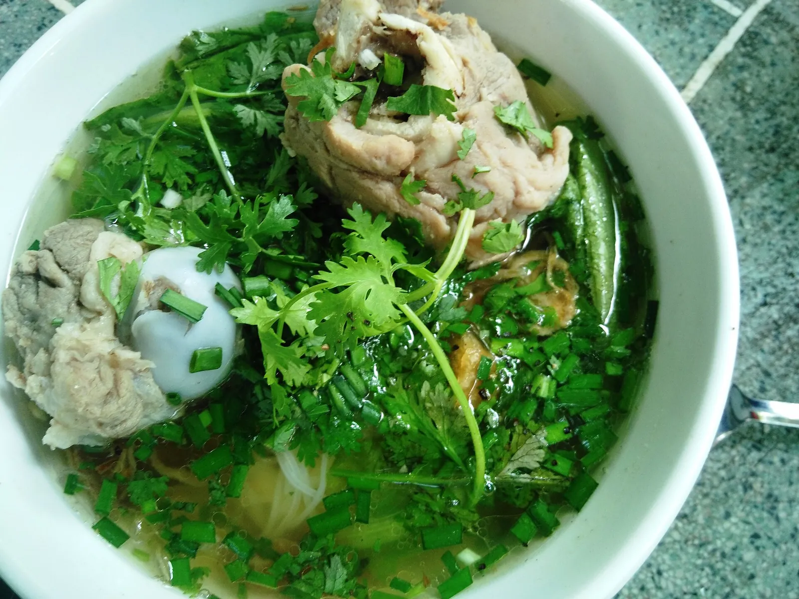 A bowl of hu tieu Nam Vang noodle soup with pork, a quail egg, chives and coriander