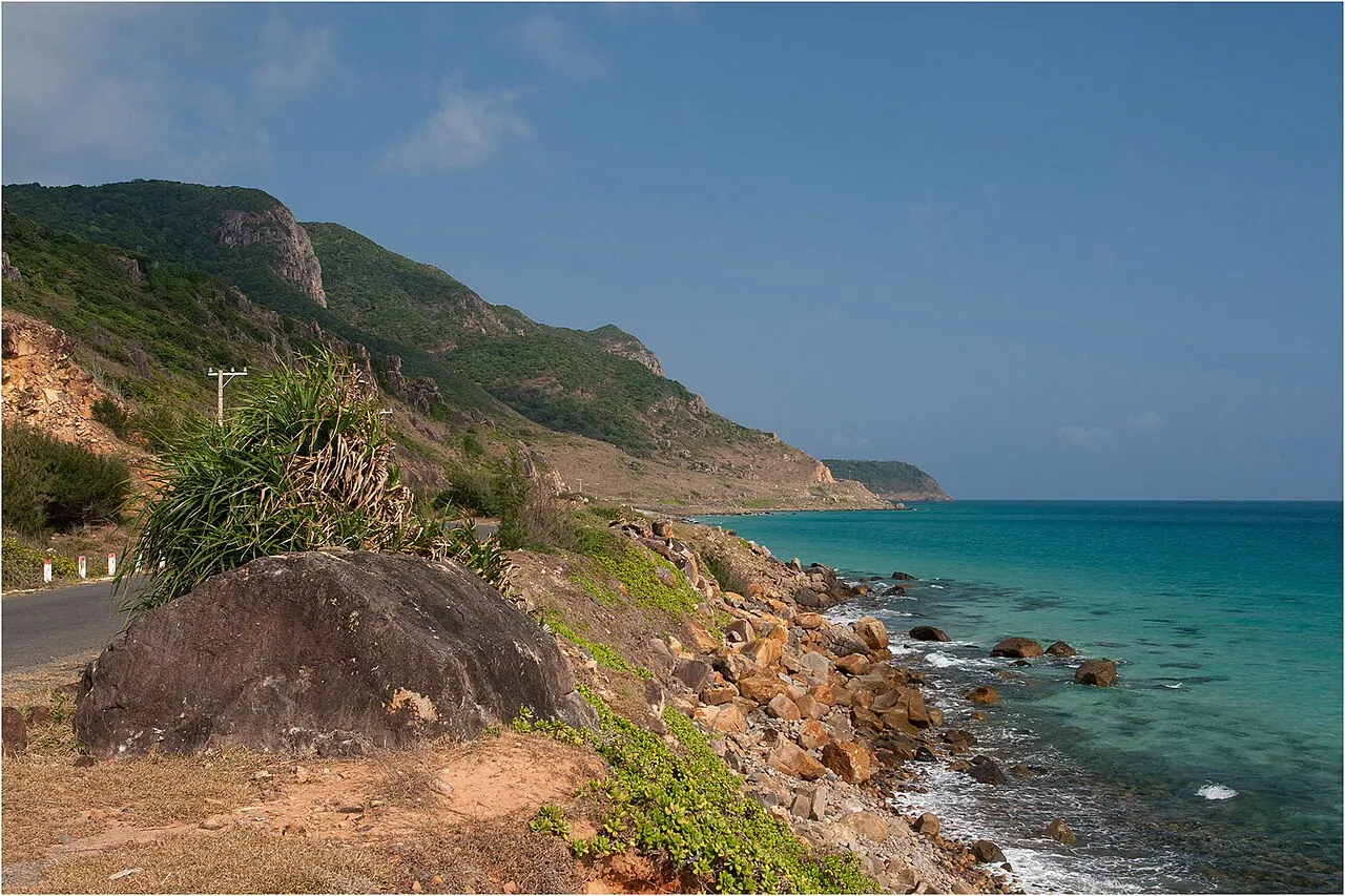 Rocky shoreline and turquoise sea beside a coastal road with green hills near Ben Dam on Con Son