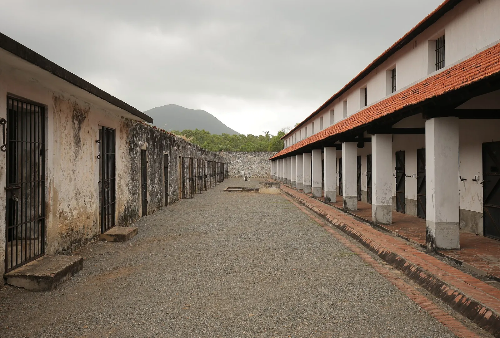 Long open courtyard between whitewashed single-storey cell blocks with red-tiled roofs at Con Dao Prison