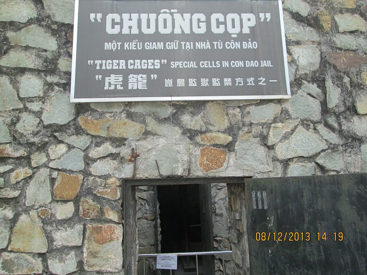 Stone wall with a sign reading Tiger Cages, special cells in Con Dao jail, above a low entrance