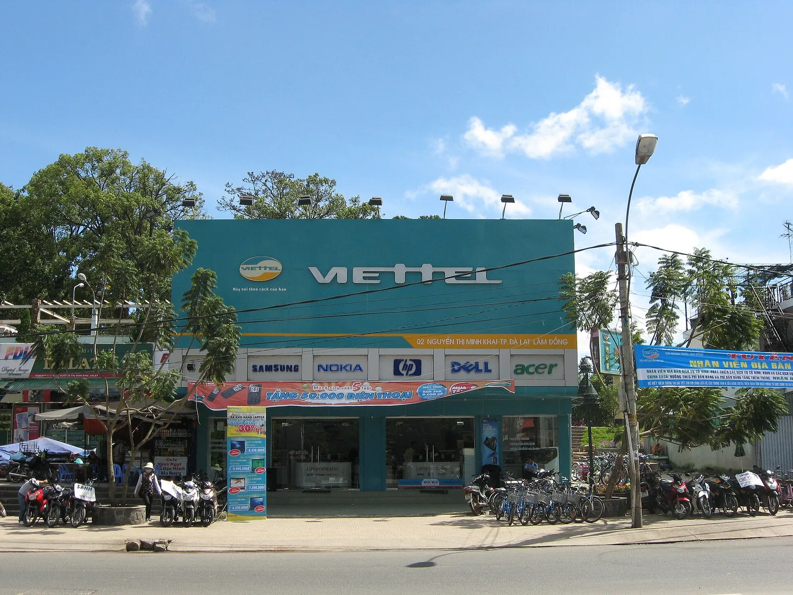 Viettel shop with its teal sign on a sunny street in Da Lat, motorbikes parked in front