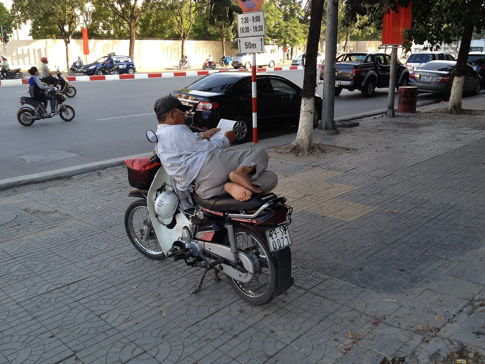 Motorbike-taxi driver sitting on his parked scooter at the kerb on Lieu Giai street, Hanoi