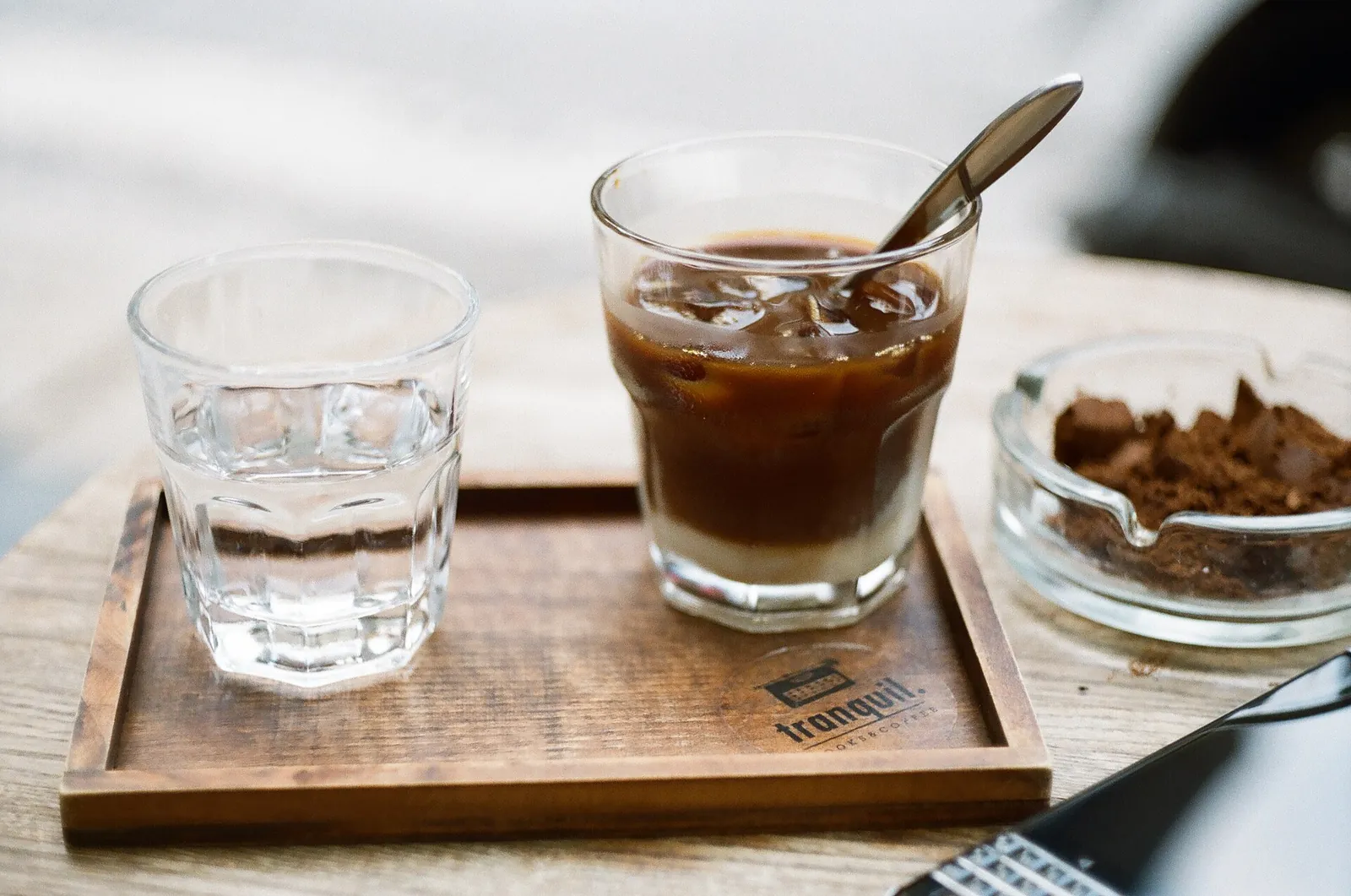 Glass of Vietnamese iced coffee with milk on a wooden tray, beside a glass of water and a dish of coffee grounds