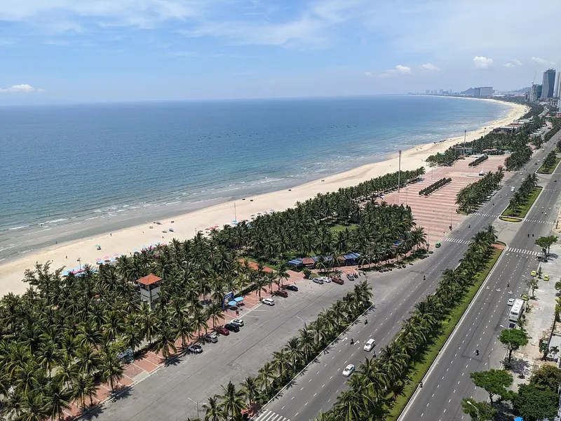 Luftfoto af My Khe Beach i Da Nang med en lang stribe lyst sand, en park med palmer og kystvejen, der løber mod nord