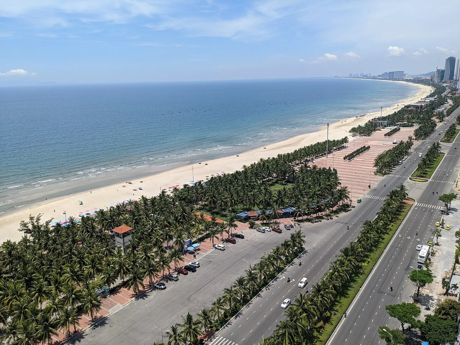 Aerial view of My Khe Beach in Da Nang, with a long strip of pale sand, palm-lined park and the coastal road running north