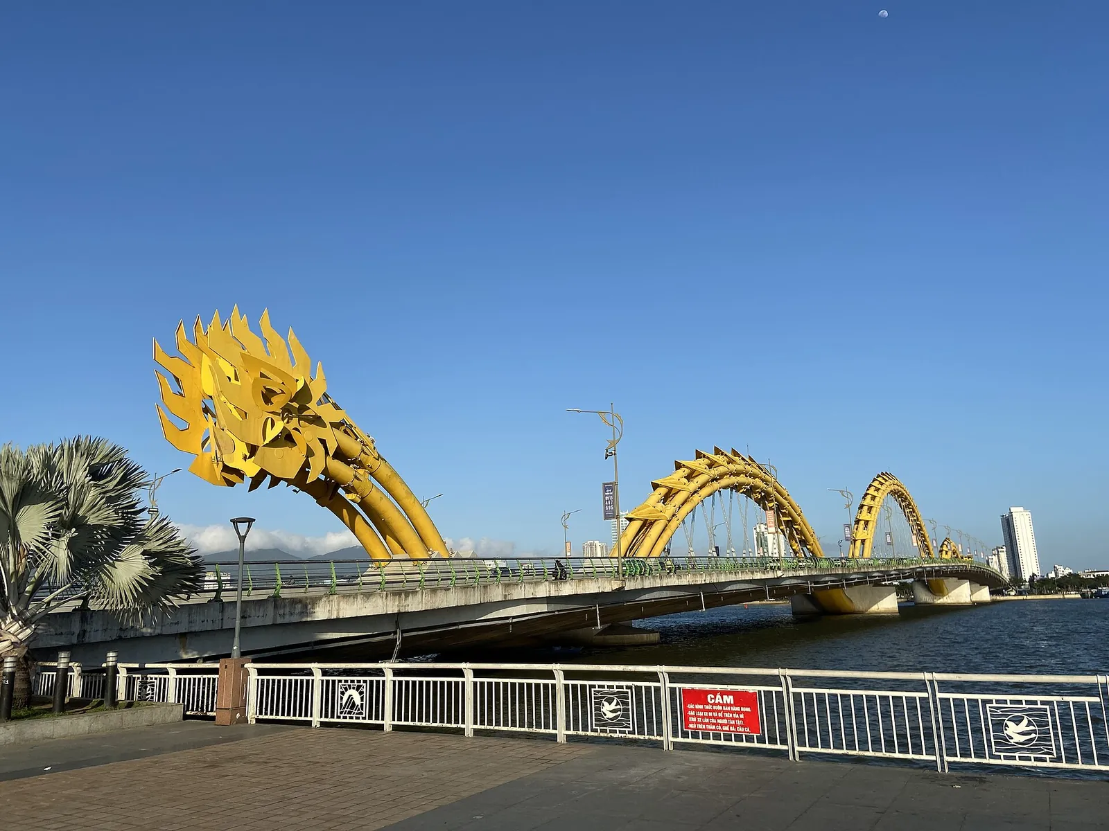 The yellow steel arches and dragon head of Dragon Bridge over the Han River in Da Nang under a blue sky