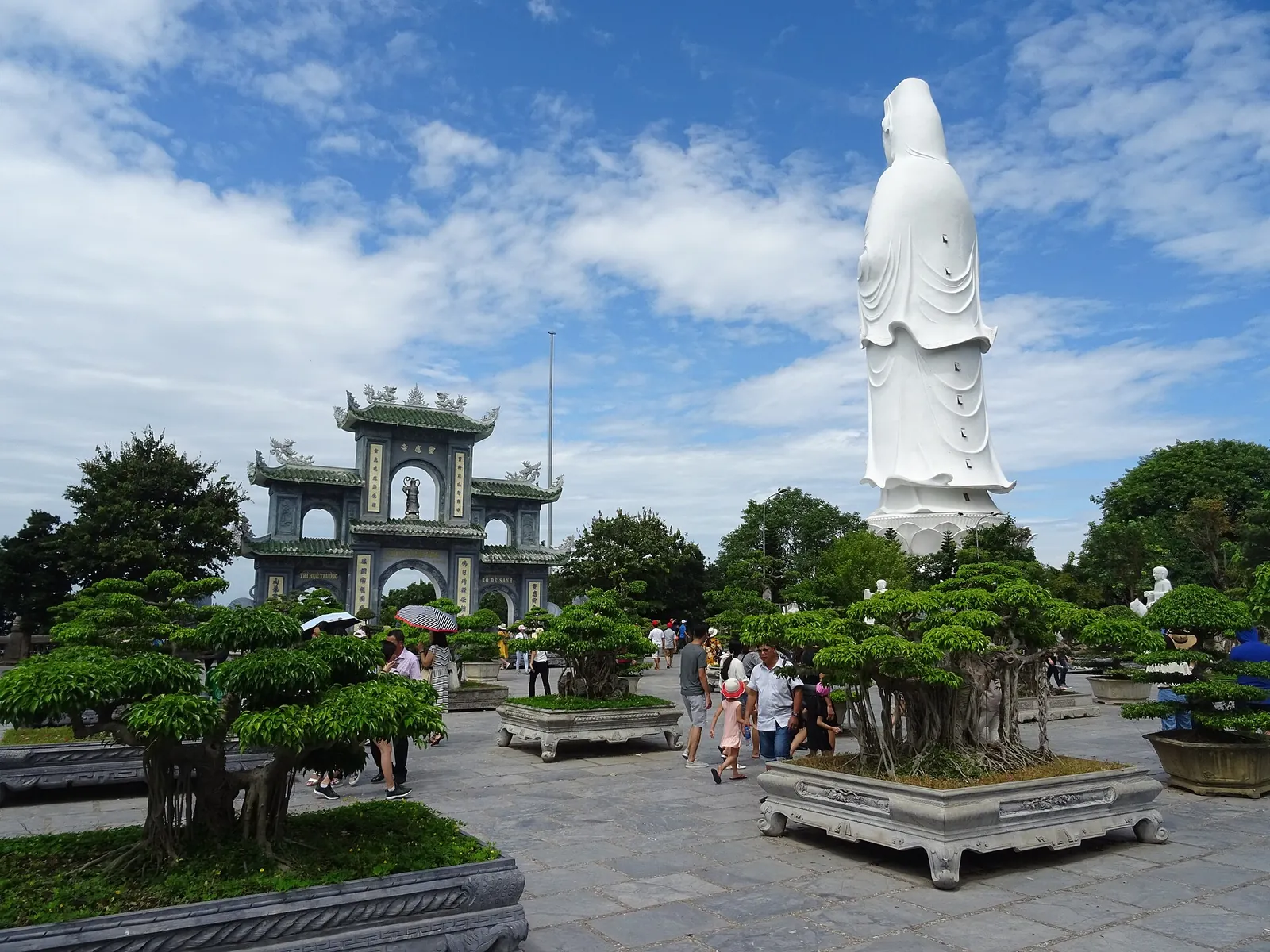White Lady Buddha statue rising above bonsai trees and a gateway at Linh Ung Pagoda on the Son Tra Peninsula, Da Nang