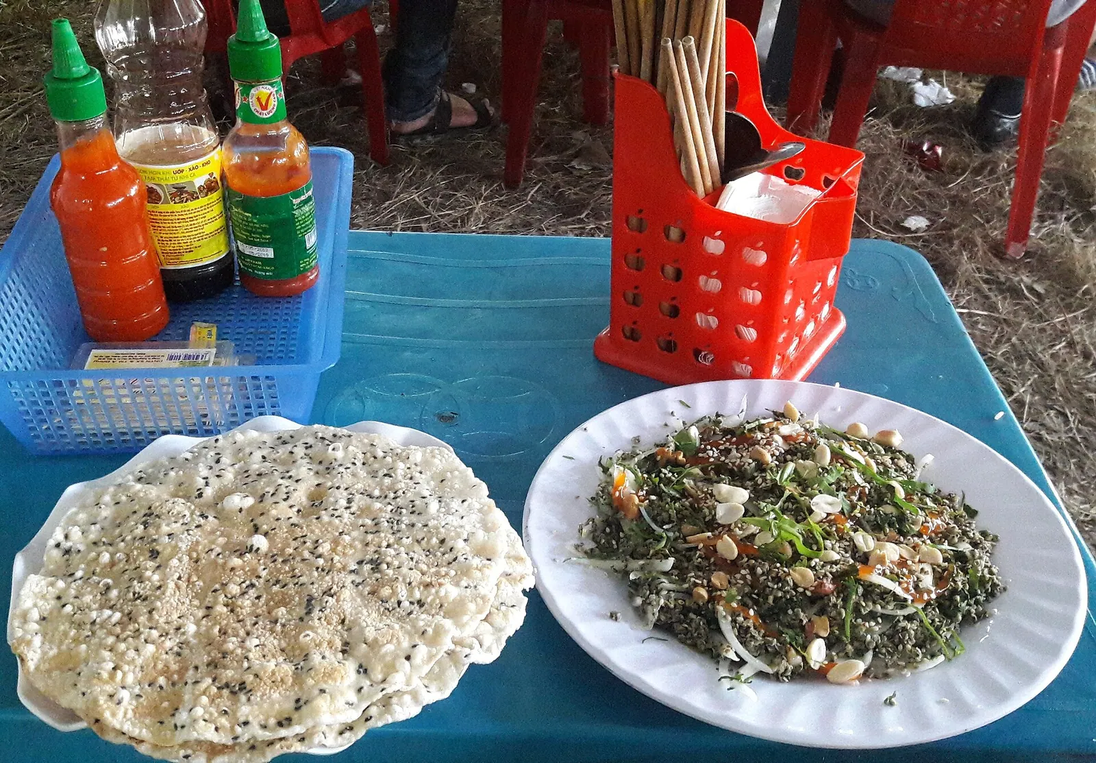 A plate of bun hen Mai Xa, noodles with stir-fried baby clams and herbs, beside a sesame rice cracker on a stall table