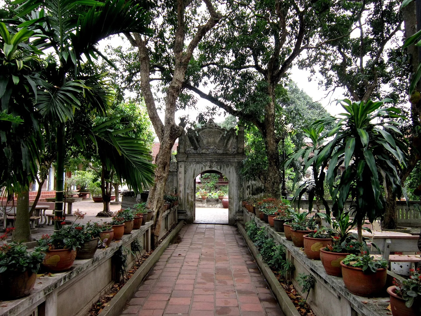 Brick-paved path between potted plants leading to the gate of Mia Pagoda