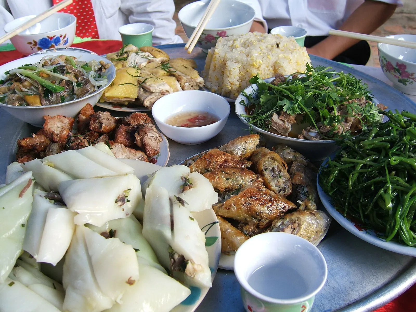 A tray of northern Vietnamese dishes with rice cakes, greens, fried rolls and dipping bowls