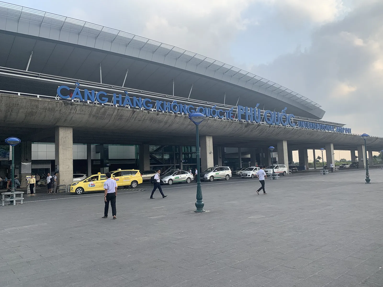 Terminal building of Phu Quoc International Airport with taxis and passengers outside under a cloudy sky