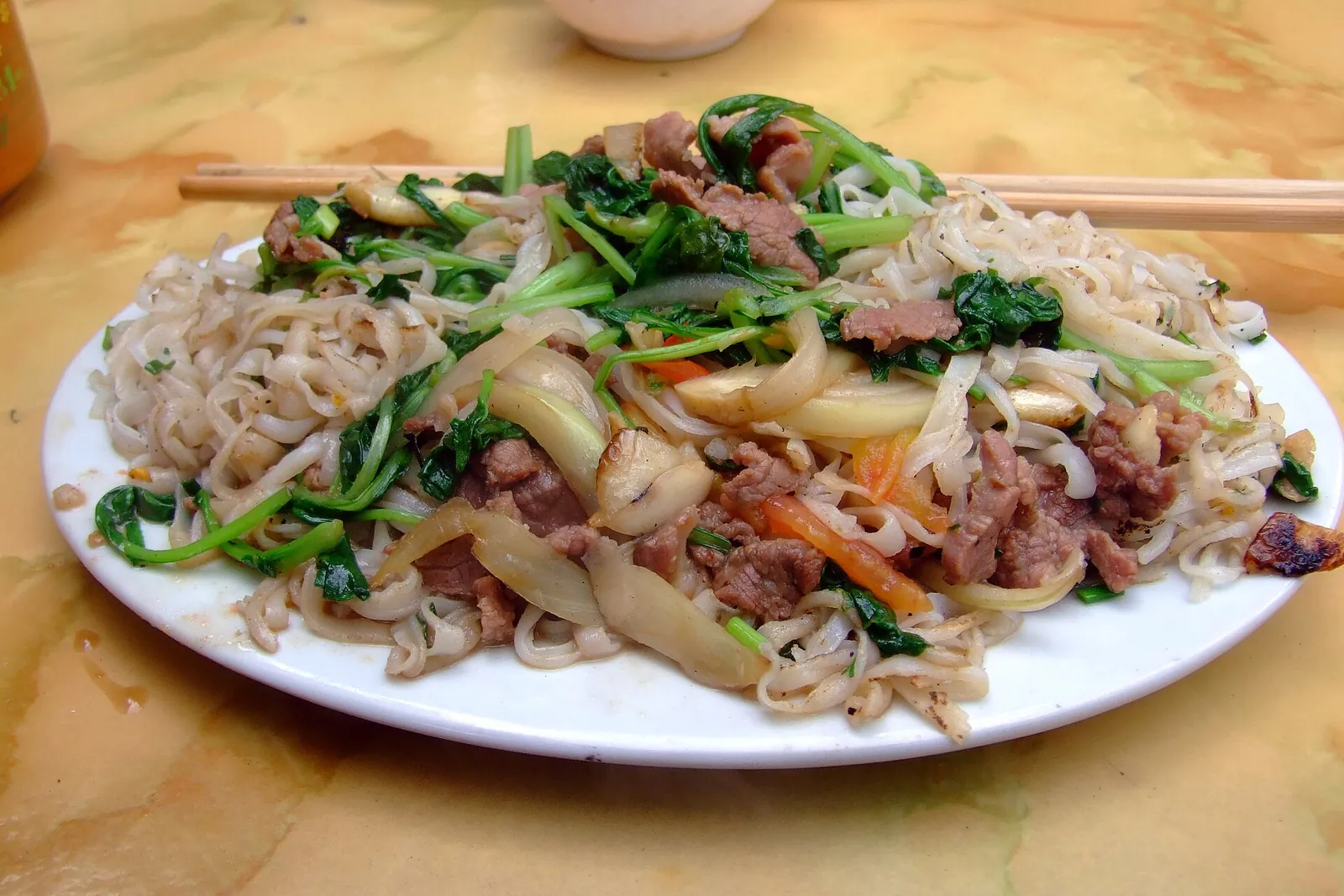 Plate of phở xào bò, stir-fried flat rice noodles with beef, morning glory and onions, on a restaurant table in Hanoi