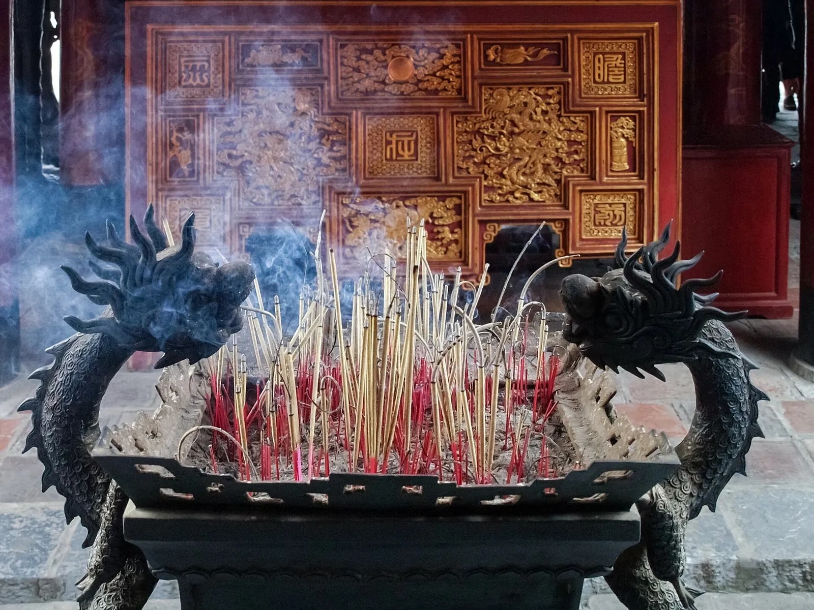 Bundles of burning incense sticks in a burner flanked by dragon heads at the Temple of Literature, Hanoi