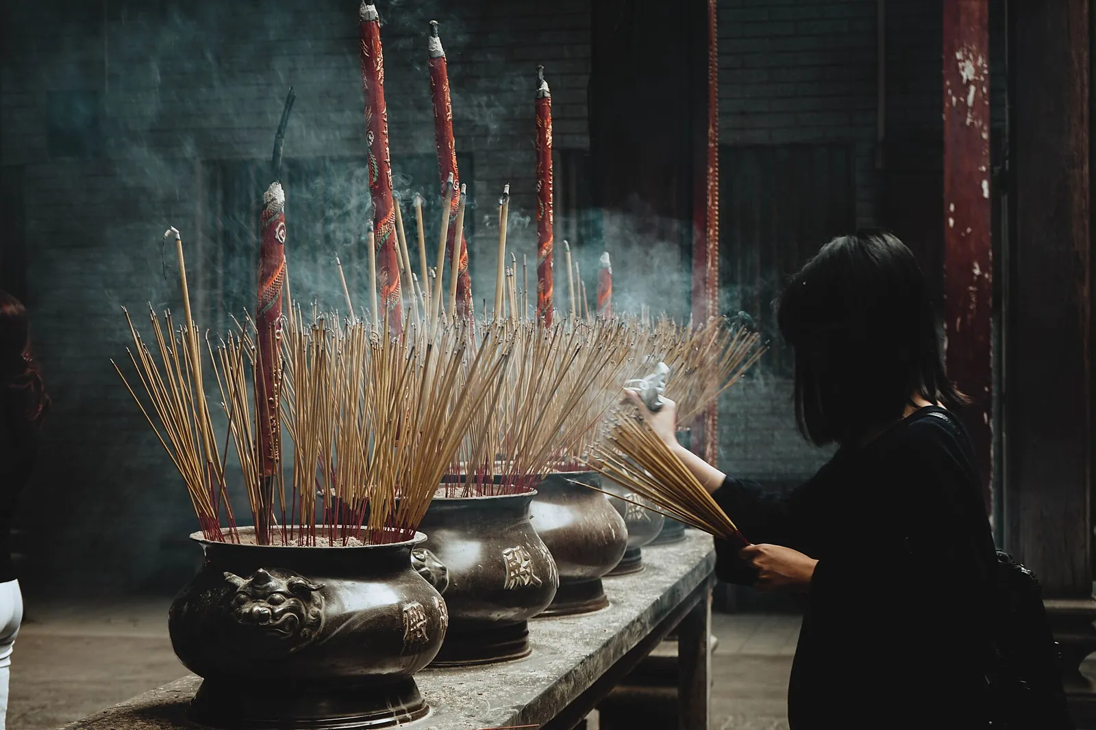 A woman standing in incense smoke beside large burners full of joss sticks at Thien Hau Temple, Ho Chi Minh City