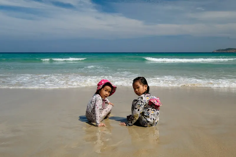 Two young girls in sun hats playing in the wet sand at the water's edge on a beach near Cam Ranh, Vietnam