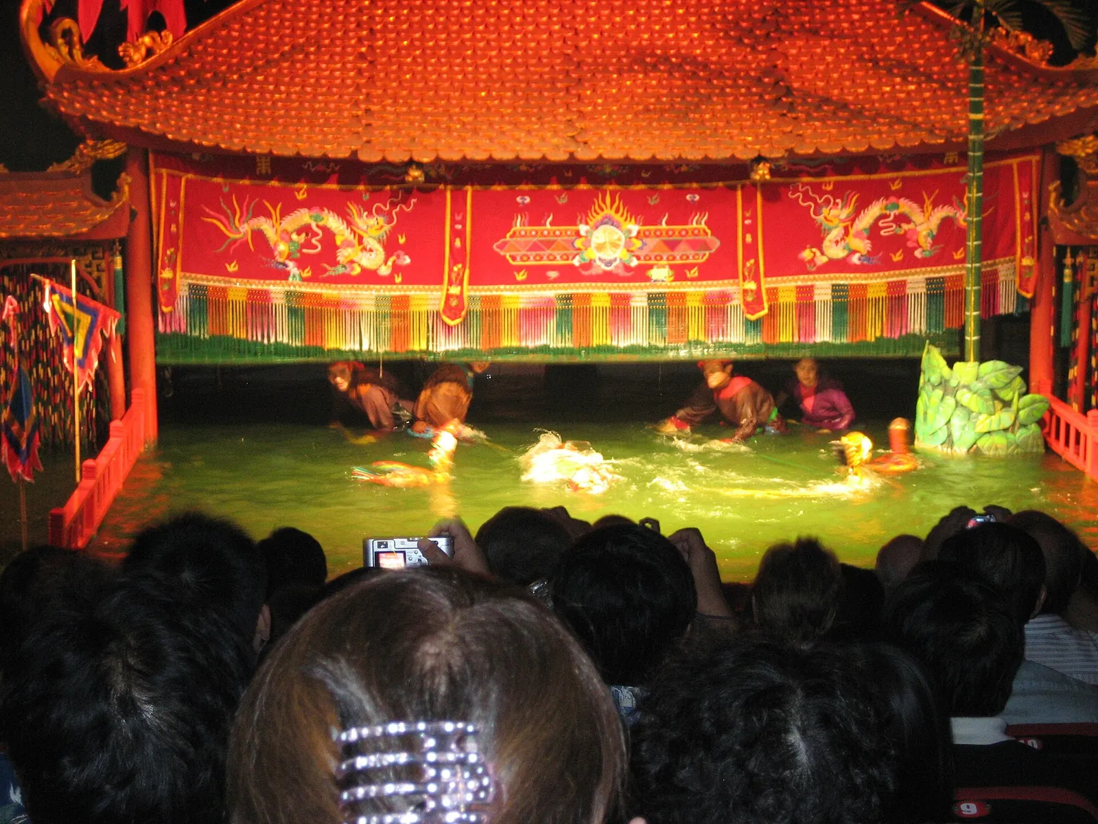 Water puppets performing on the water stage of a theatre in Hanoi, with the audience in the foreground