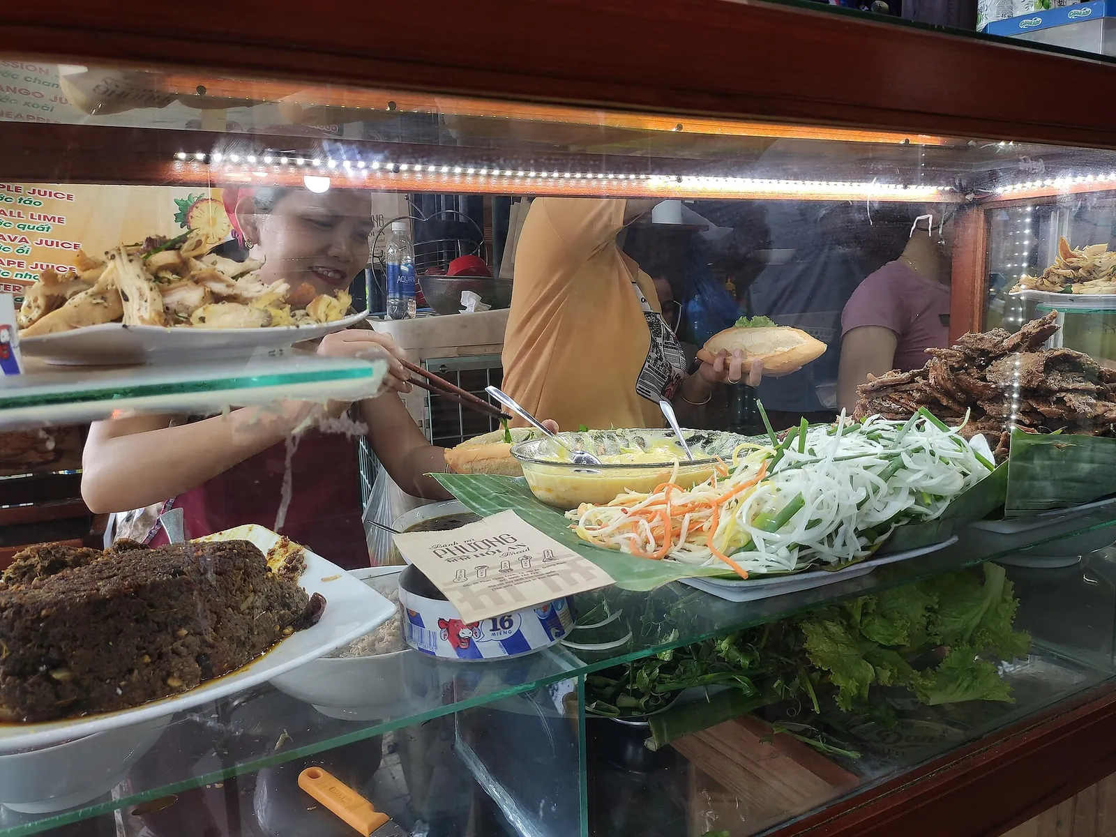 The counter of Banh Mi Phuong in Hoi An, with fillings, herbs and pickles laid out as staff assemble sandwiches
