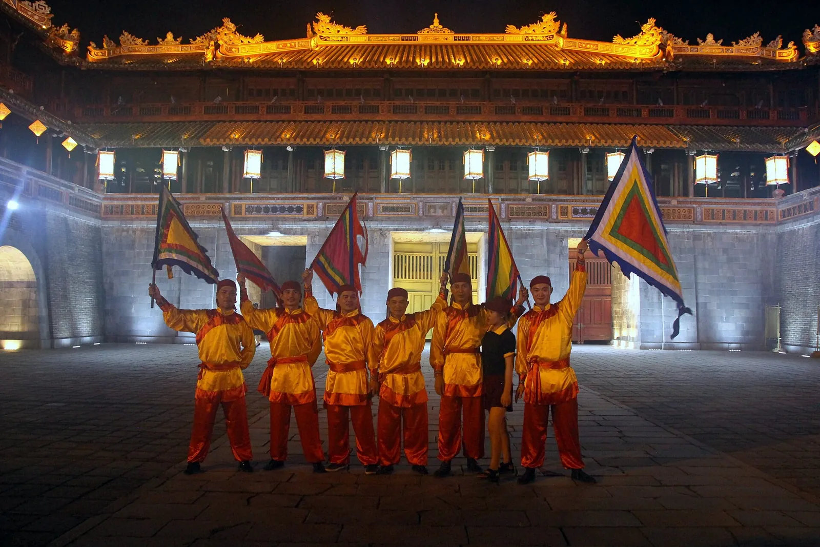 Performers in yellow costumes holding banners in front of the illuminated Imperial City in Hue at night