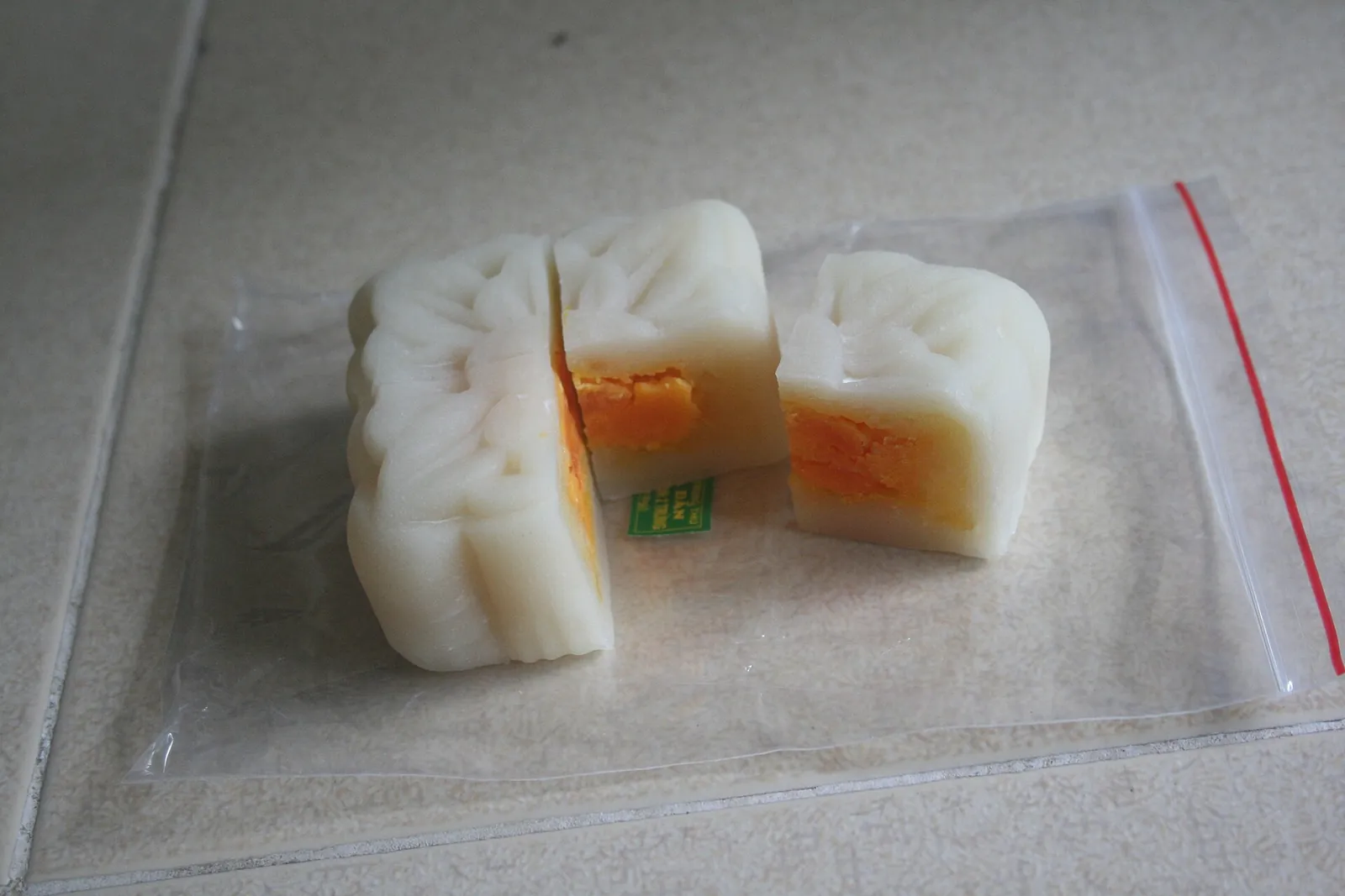 Two white bánh dẻo mooncakes, one cut open to show a mung bean filling with a salted egg yolk