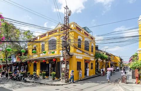 Gule rækkehuse med grønne lanterner på et gadehjørne i Hoi An gamle by under en blå himmel