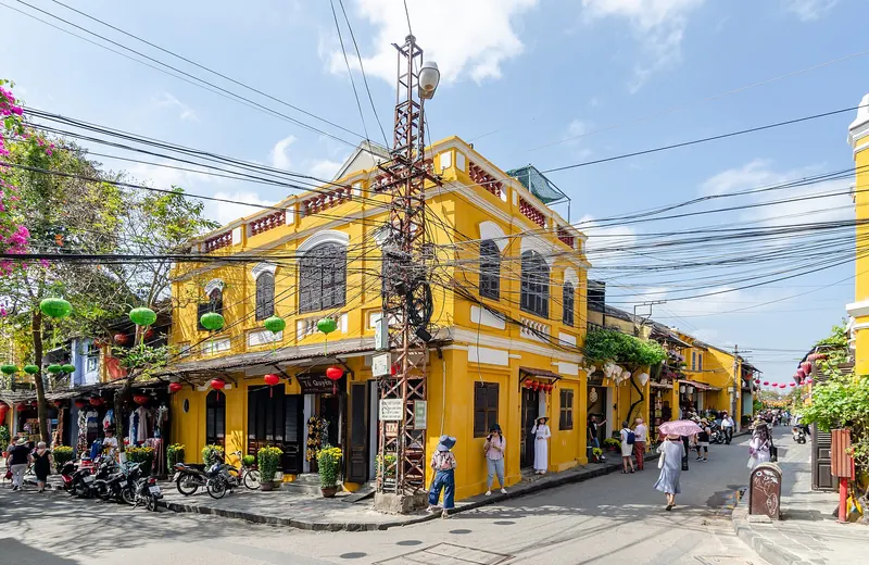 Yellow shophouses with green lanterns at a street corner in Hoi An Ancient Town under a blue sky