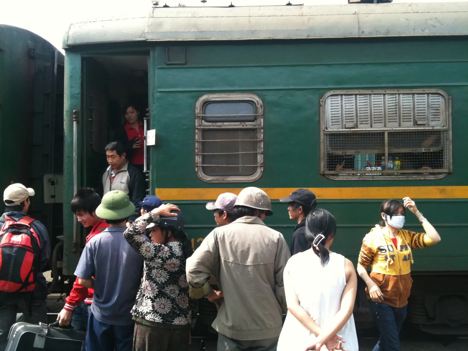 Passengers stepping down from a green Reunification Express carriage onto a station platform