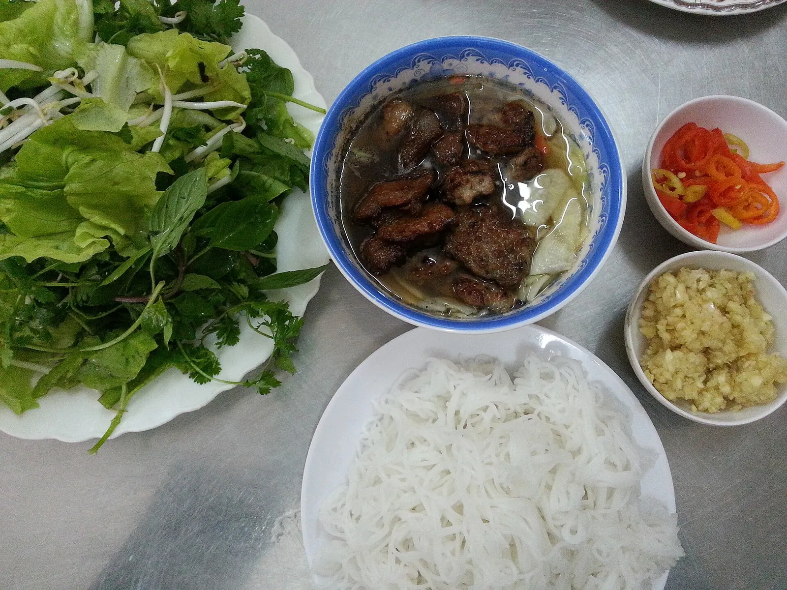 Bún chả in Hanoi: grilled pork in broth with rice vermicelli, a plate of herbs, chilli and garlic