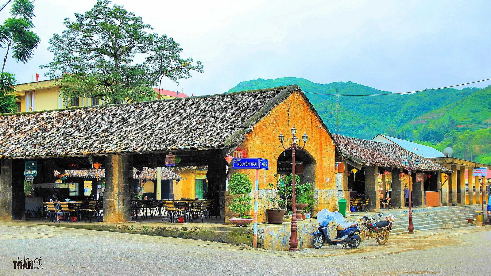 A low tiled-roof market building with yellow walls and arched openings beside a quiet street