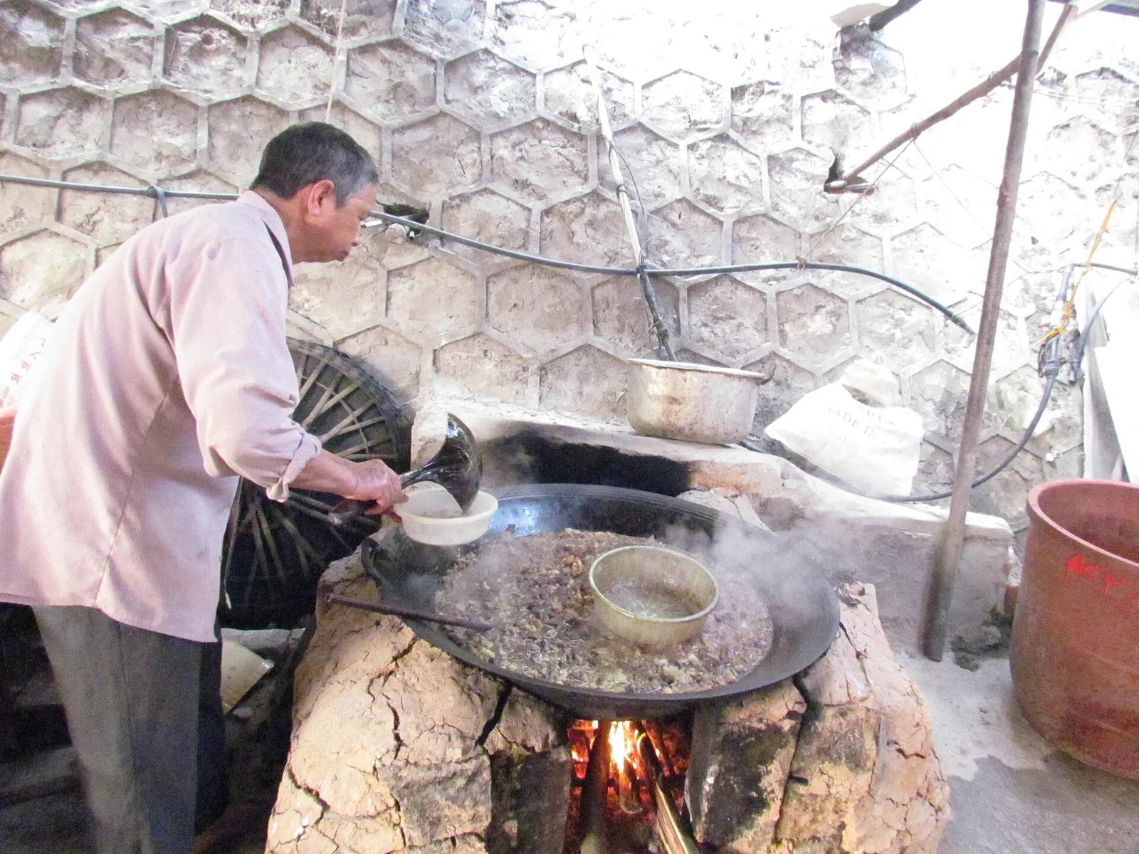 A cook stirring a large pan of thang co stew over a wood fire