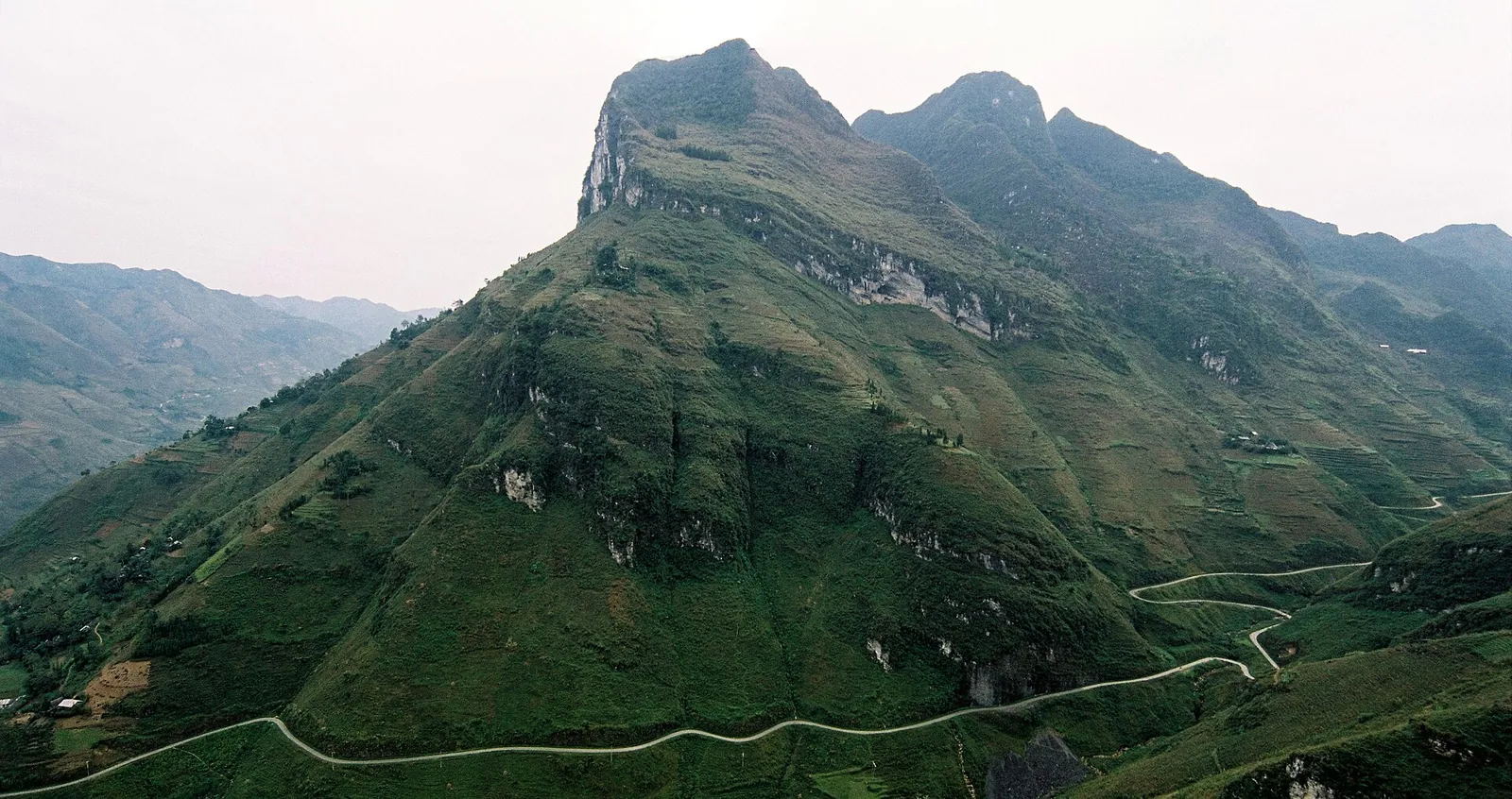 The road winding along the green mountainside below a limestone peak at the Ma Pi Leng Pass