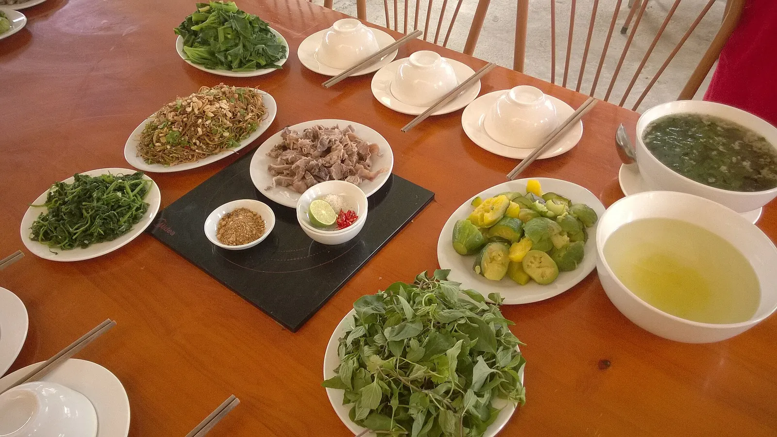 A table of local dishes in Ha Giang city: bowls of soup, plates of greens and herbs, sliced vegetables and a small plate of meat