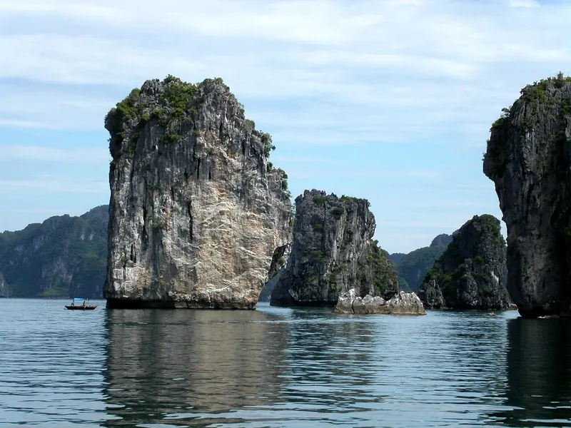 Tall limestone karst islets rising from calm water in Ha Long Bay under a blue sky