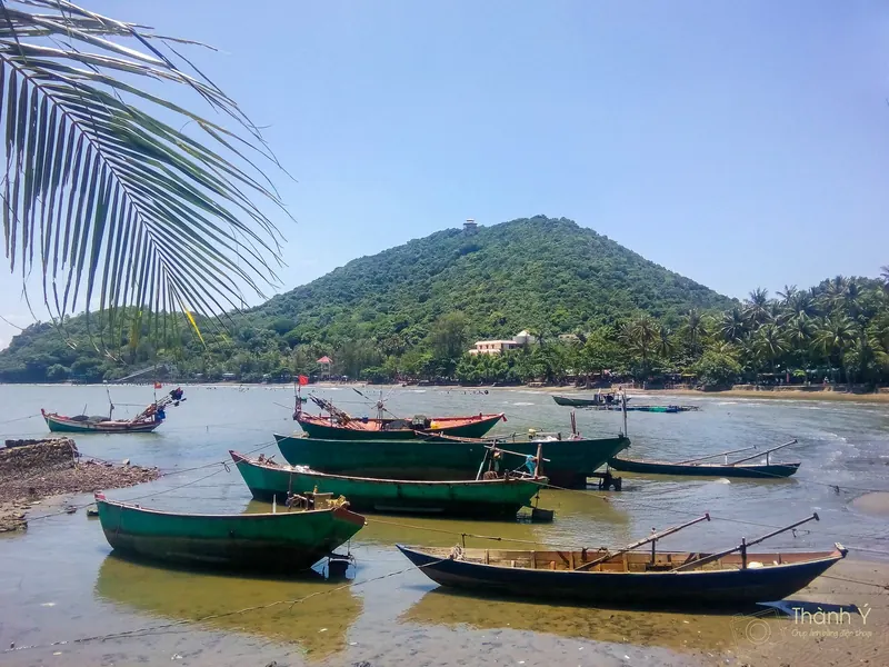Wooden fishing boats moored in the shallows at Mui Nai, Ha Tien, below a green forested hill