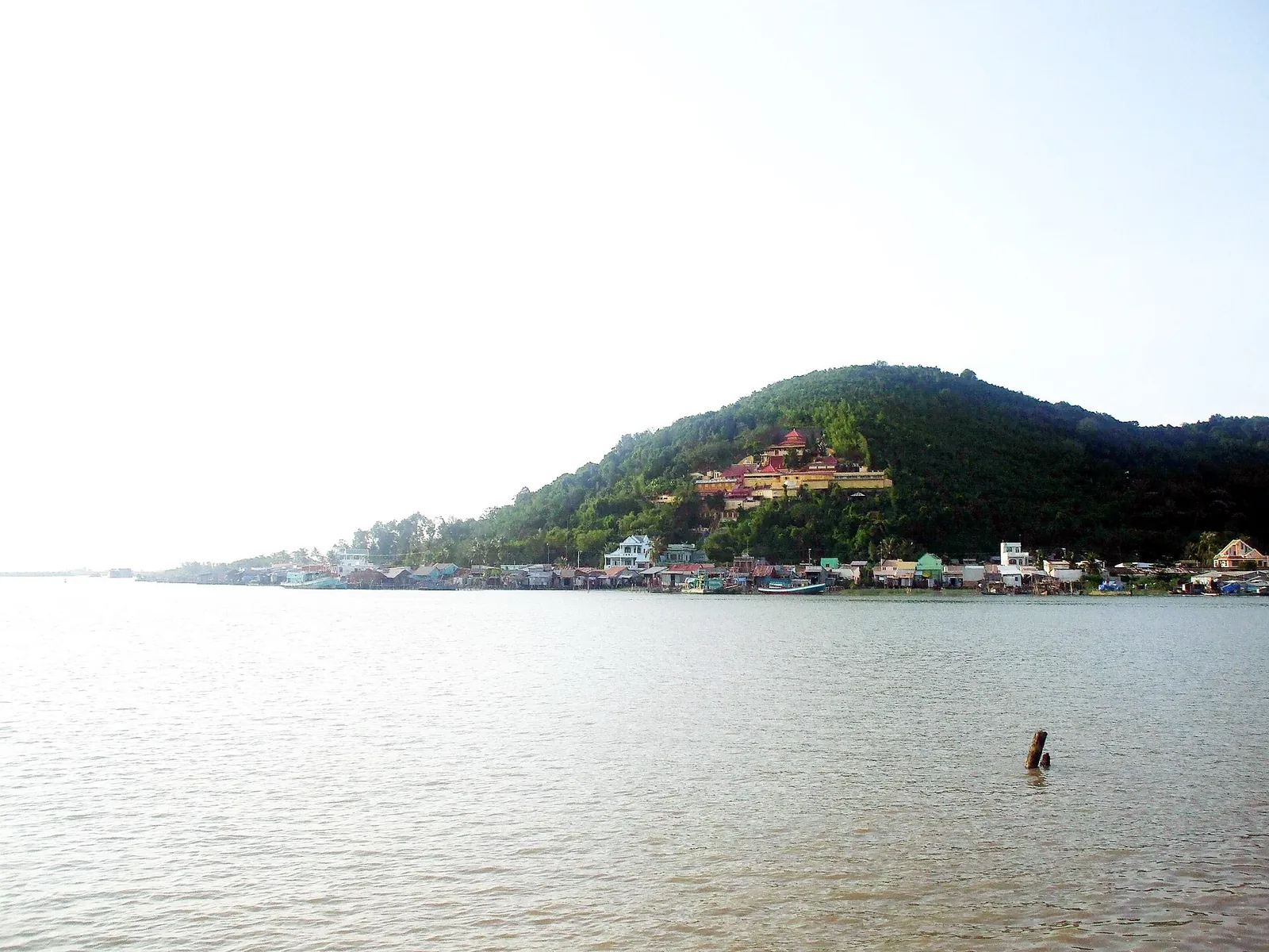 The wide calm water of the Dong Ho lagoon with a wooded hill and a pagoda on the far shore, Ha Tien