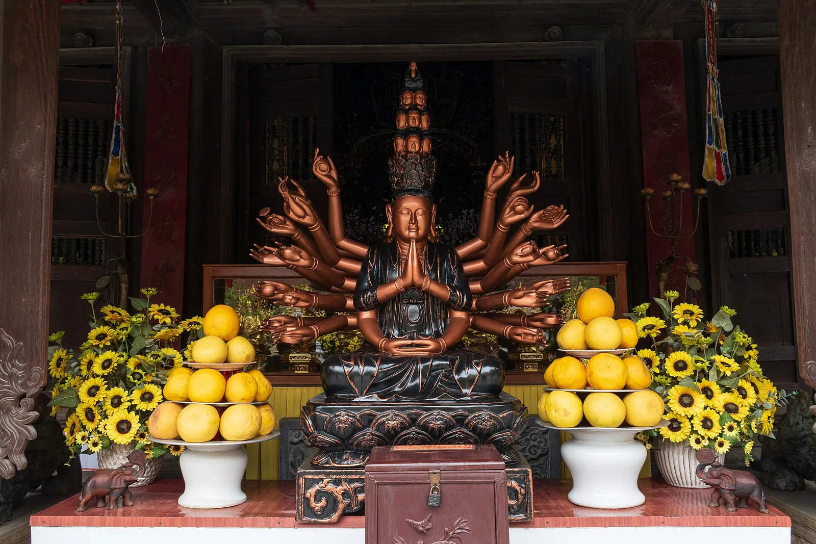 Statue of the Thousand-Armed Avalokiteshvara on an altar with sunflowers and offerings of fruit at Du Hang Pagoda