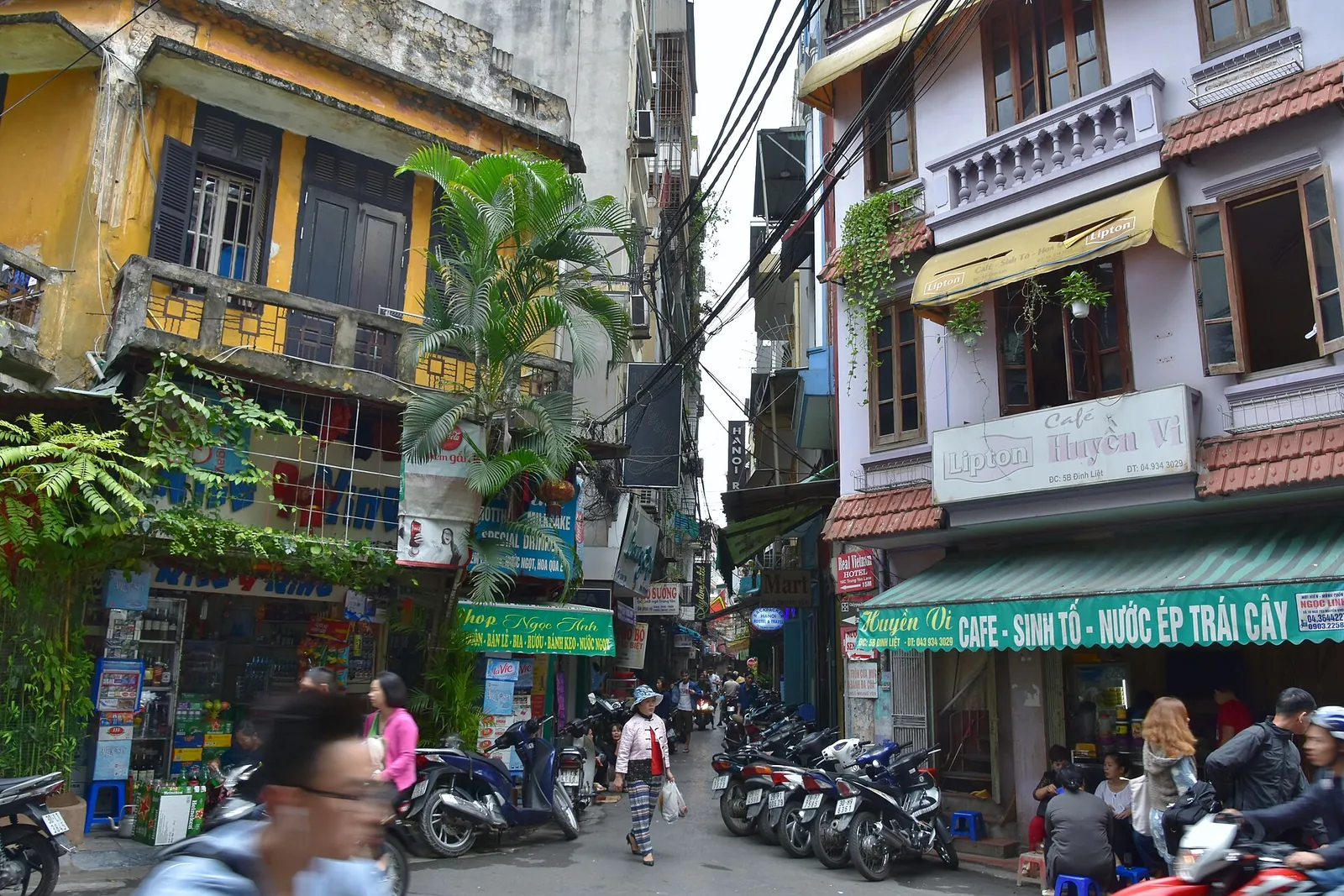 Narrow Old Quarter street in Hanoi lined with tall tube houses, shop signs and parked motorbikes