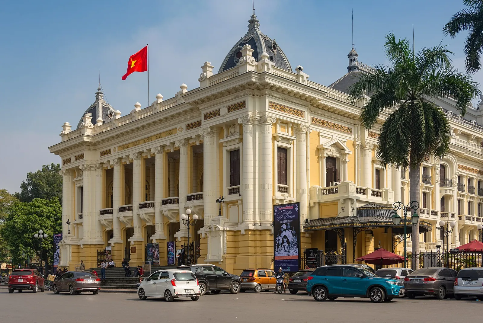 Cream-and-yellow facade of the Hanoi Opera House under a blue sky with a red flag on top