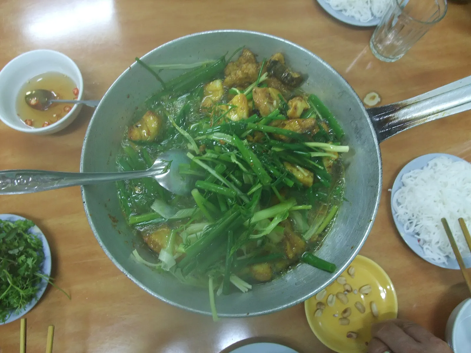 A pan of cha ca with turmeric fish and dill, served with rice noodles and herbs at Cha Ca La Vong in Hanoi