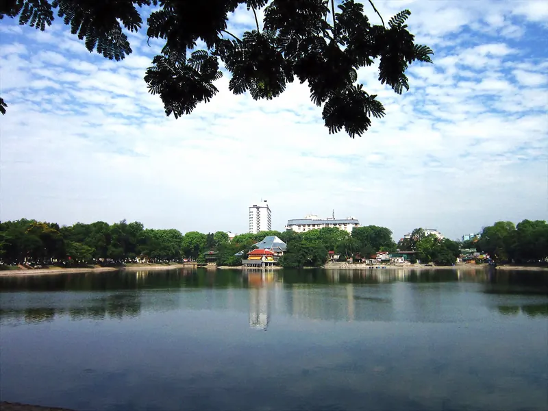 Thien Quang Lake in central Hanoi under a blue sky, with trees and buildings reflected in the still water