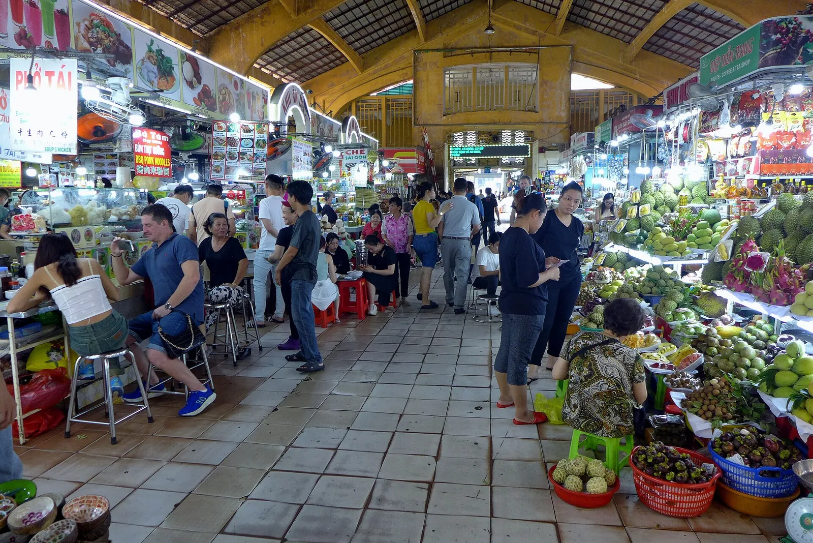 Aisles of fruit, dried goods and souvenir stalls under the roof of Ben Thanh Market, with shoppers and vendors