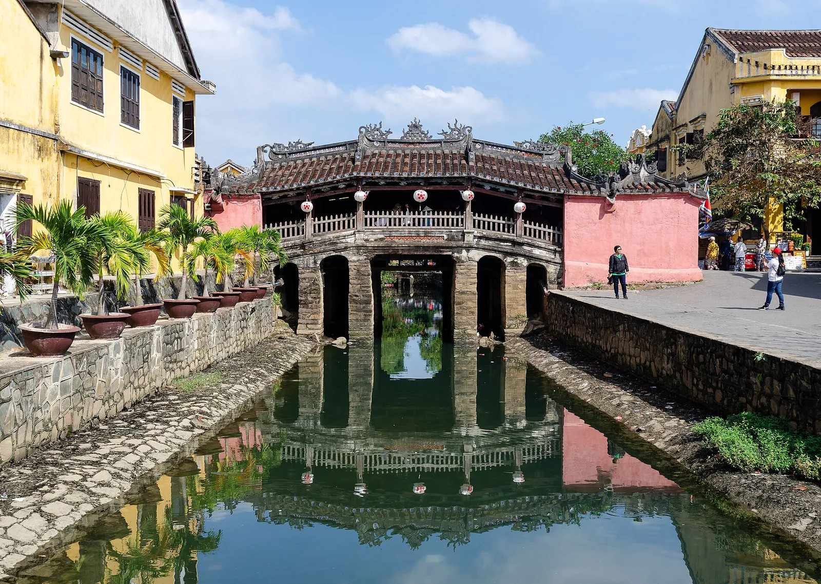 The Japanese Covered Bridge (Chùa Cầu) in Hoi An reflected in the canal beneath it, with yellow houses on either side