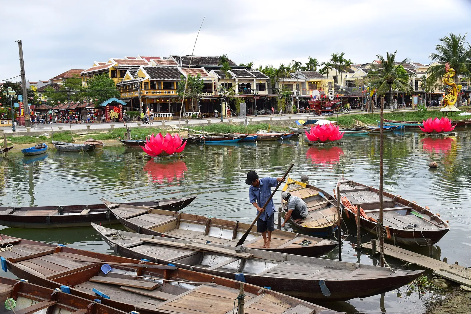 Wooden rowing boats moored on the Thu Bon River in Hoi An, with riverside houses and lotus lanterns behind