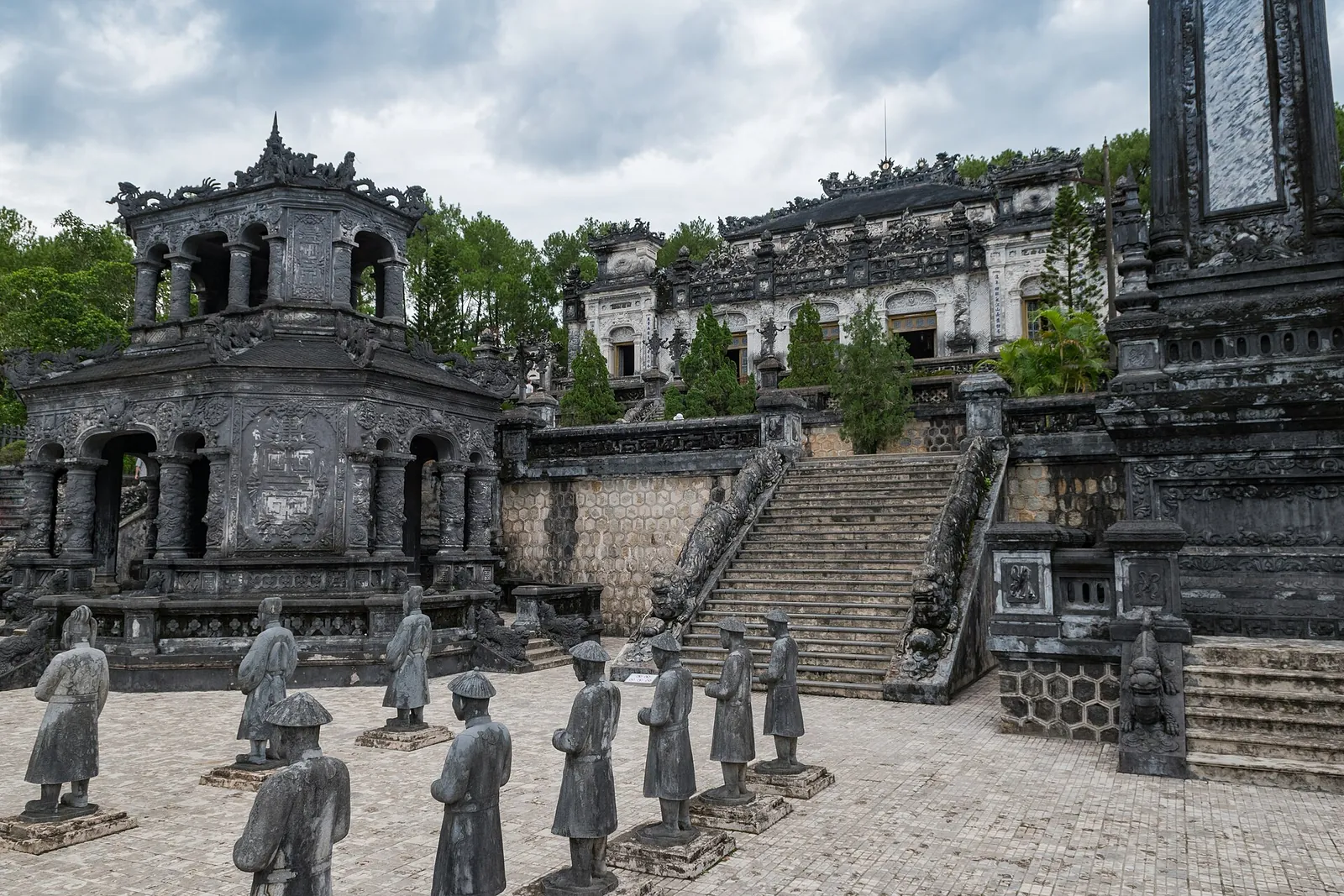 Rows of grey stone mandarin statues in the courtyard below the dark stone buildings of Khai Dinh's tomb