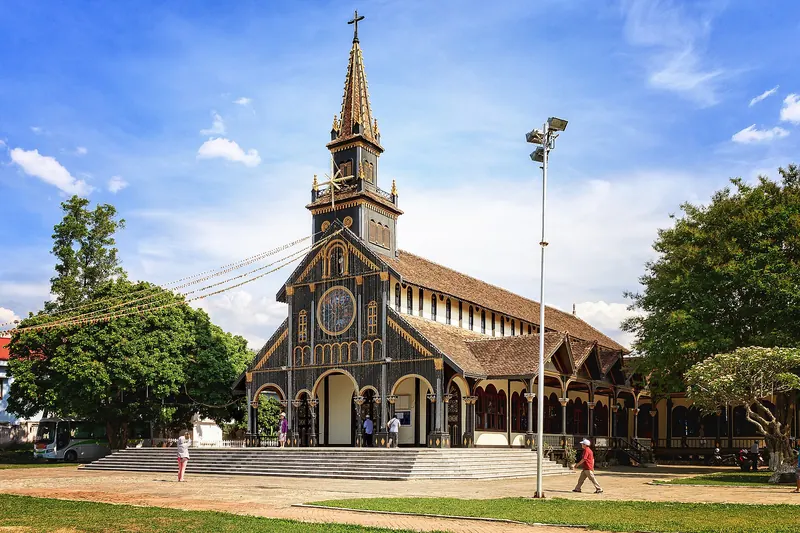 The wooden Kon Tum Cathedral with its tall cross tower and dark timber walls under a blue sky