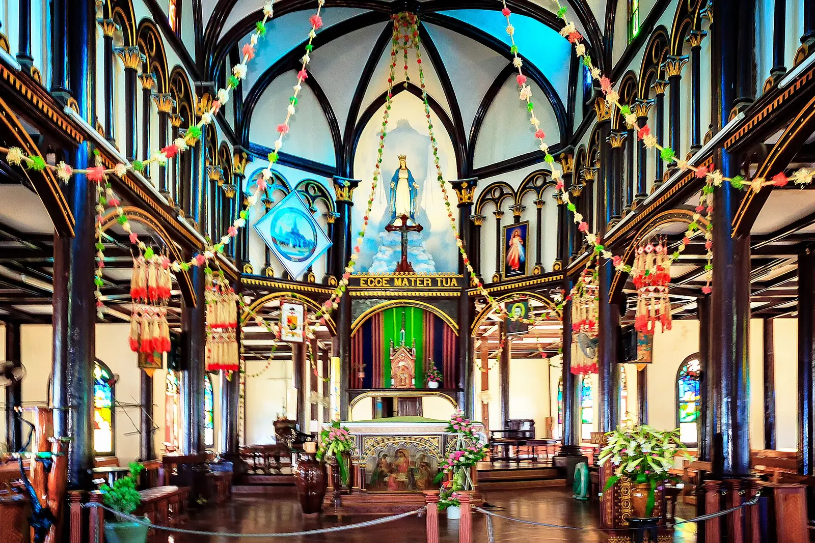 Interior of the Kon Tum wooden church with rows of dark wooden columns, arches and the decorated altar